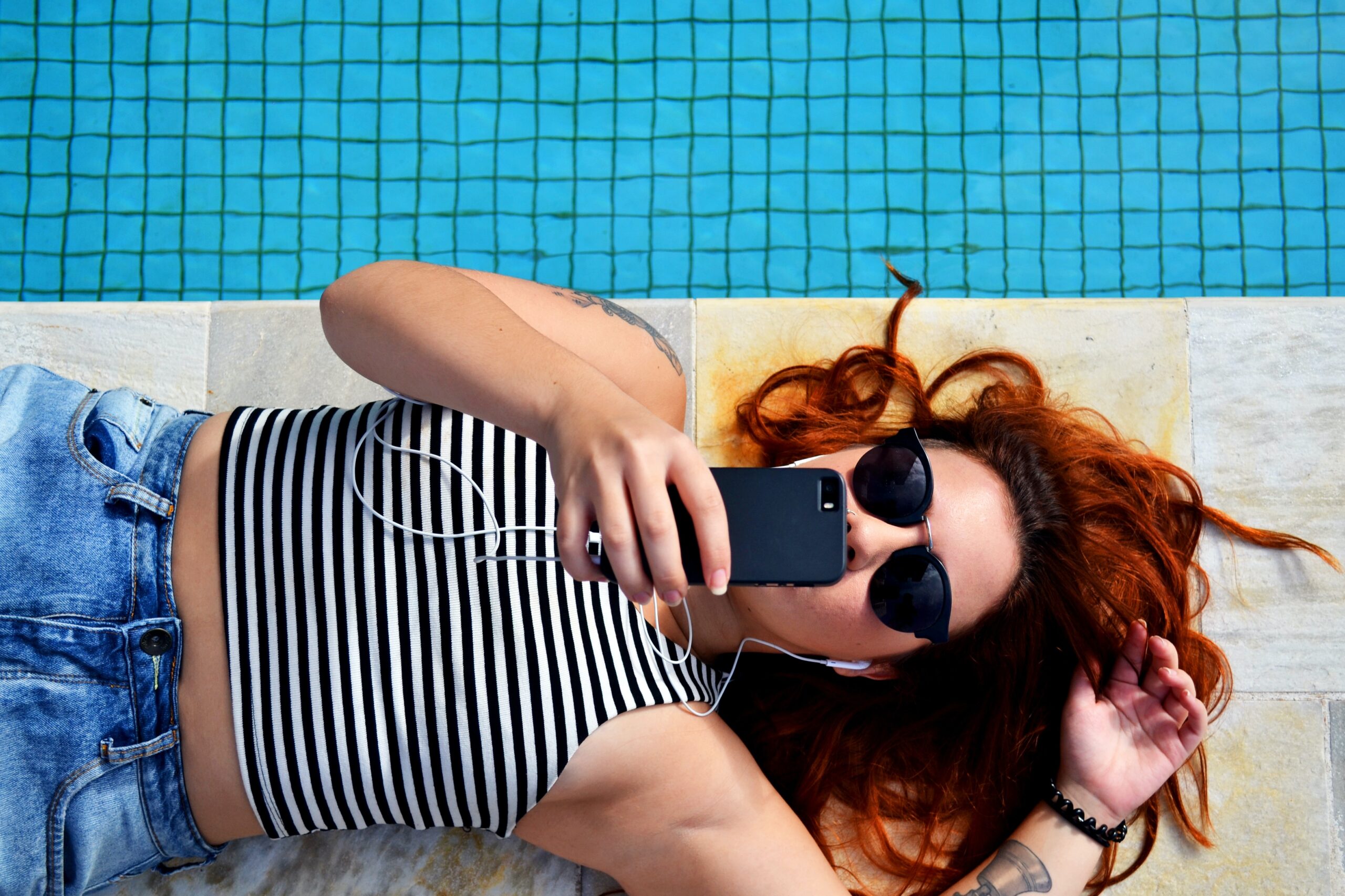 Girl laying by a pool using a phone to scroll and listen to music